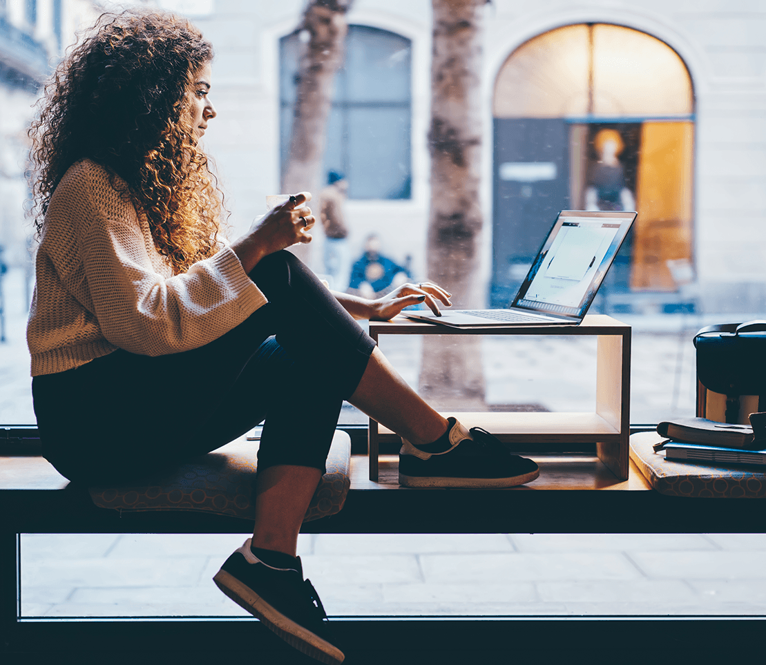 Woman sitting on a bench in a coffee shop working on a laptop