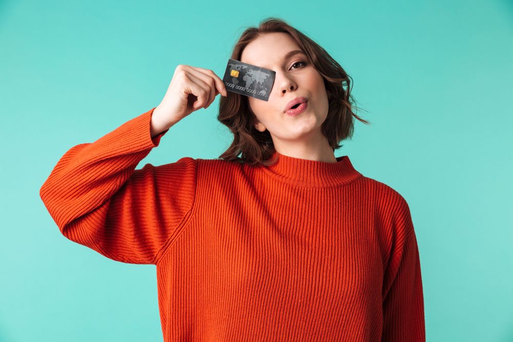 A woman in a red sweater holds a credit card over her eye.